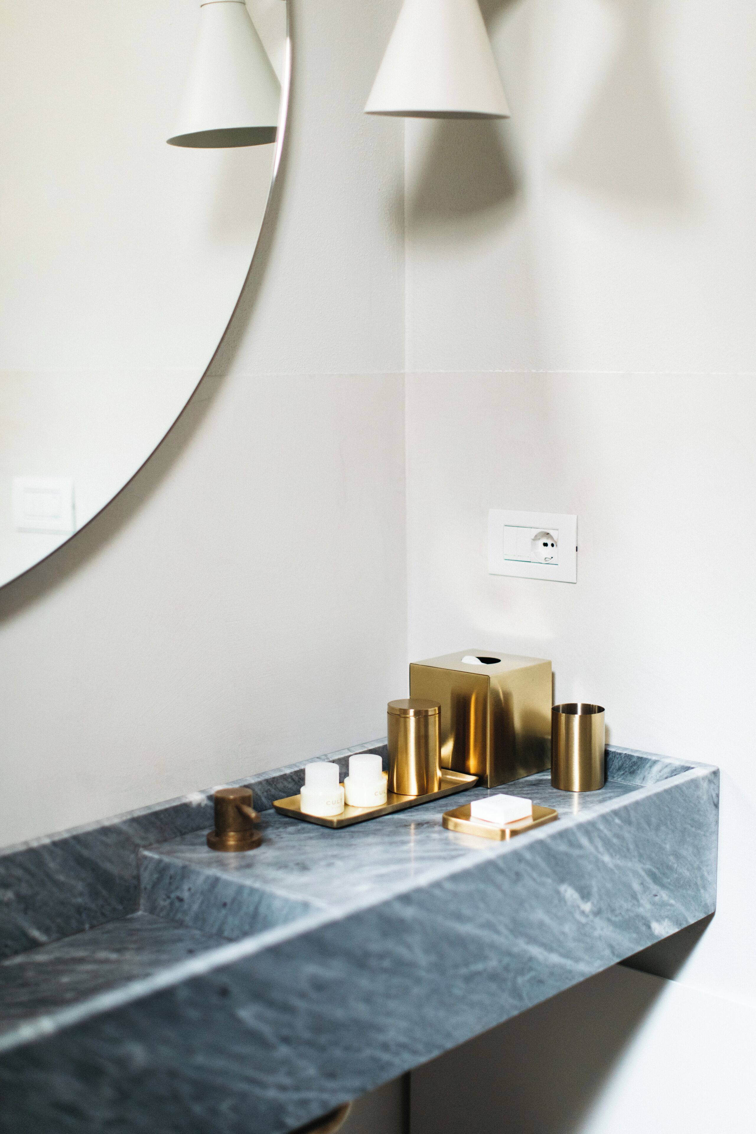 A bathroom with a marble countertop, a round mirror, and a wall-mounted light fixture.