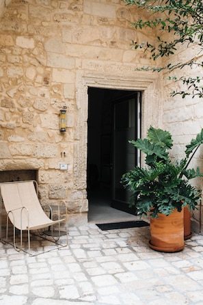 A stone building entrance with a metal chair and a large potted plant.