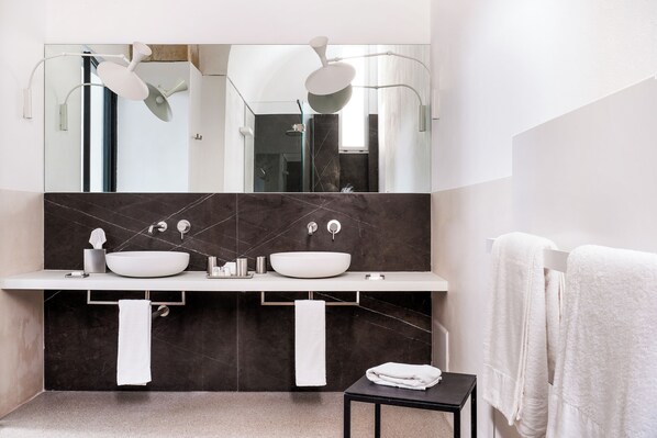 A modern bathroom with two sinks, a large mirror, and a small table with towels. - Palazzo De Noha (Lecce)