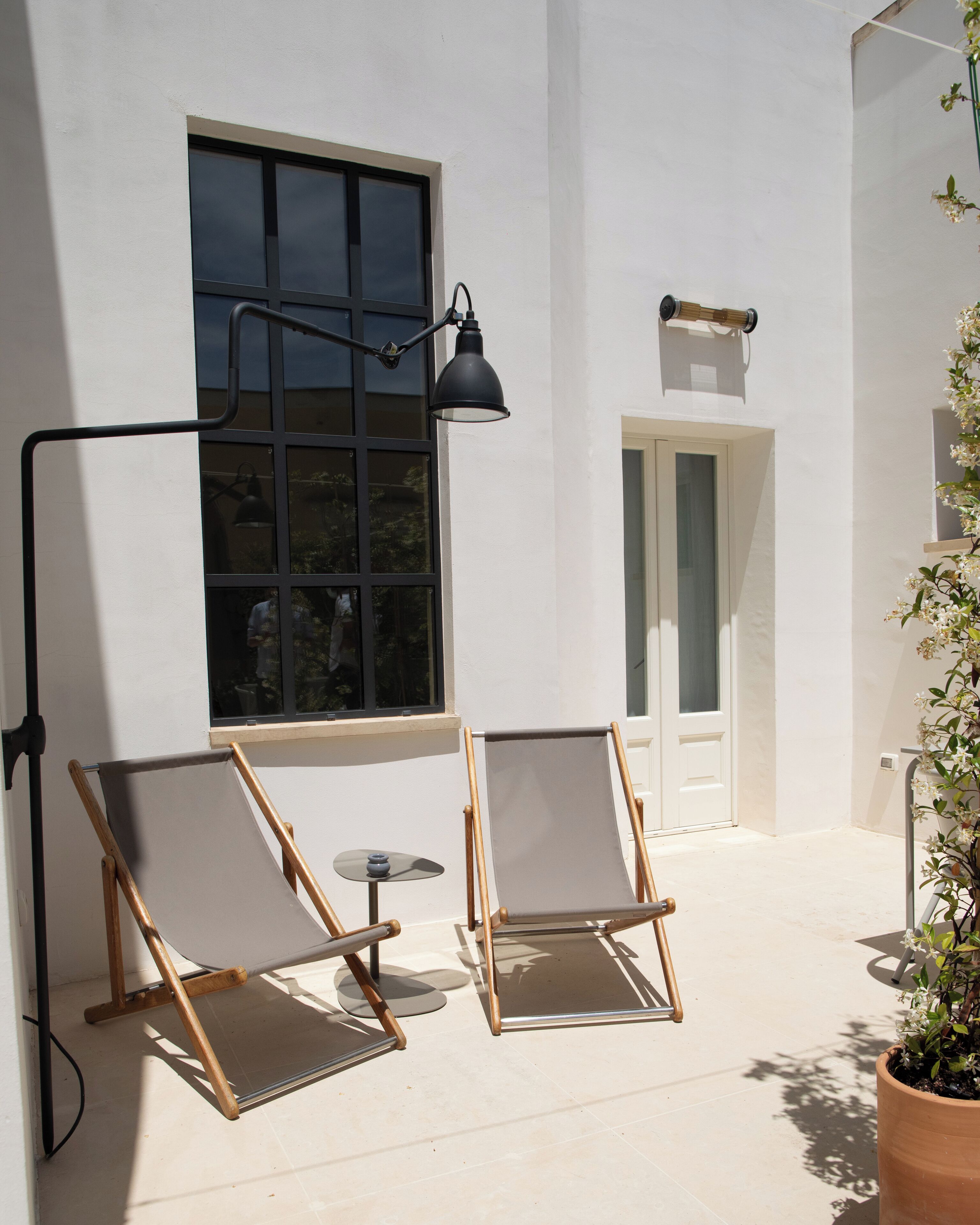 Un patio con dos sillones de madera, una mesita, una planta en maceta y una puerta al fondo.