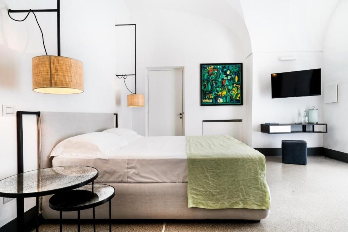 A modern bedroom with a bed, a small round table, a television, and a colorful abstract painting.