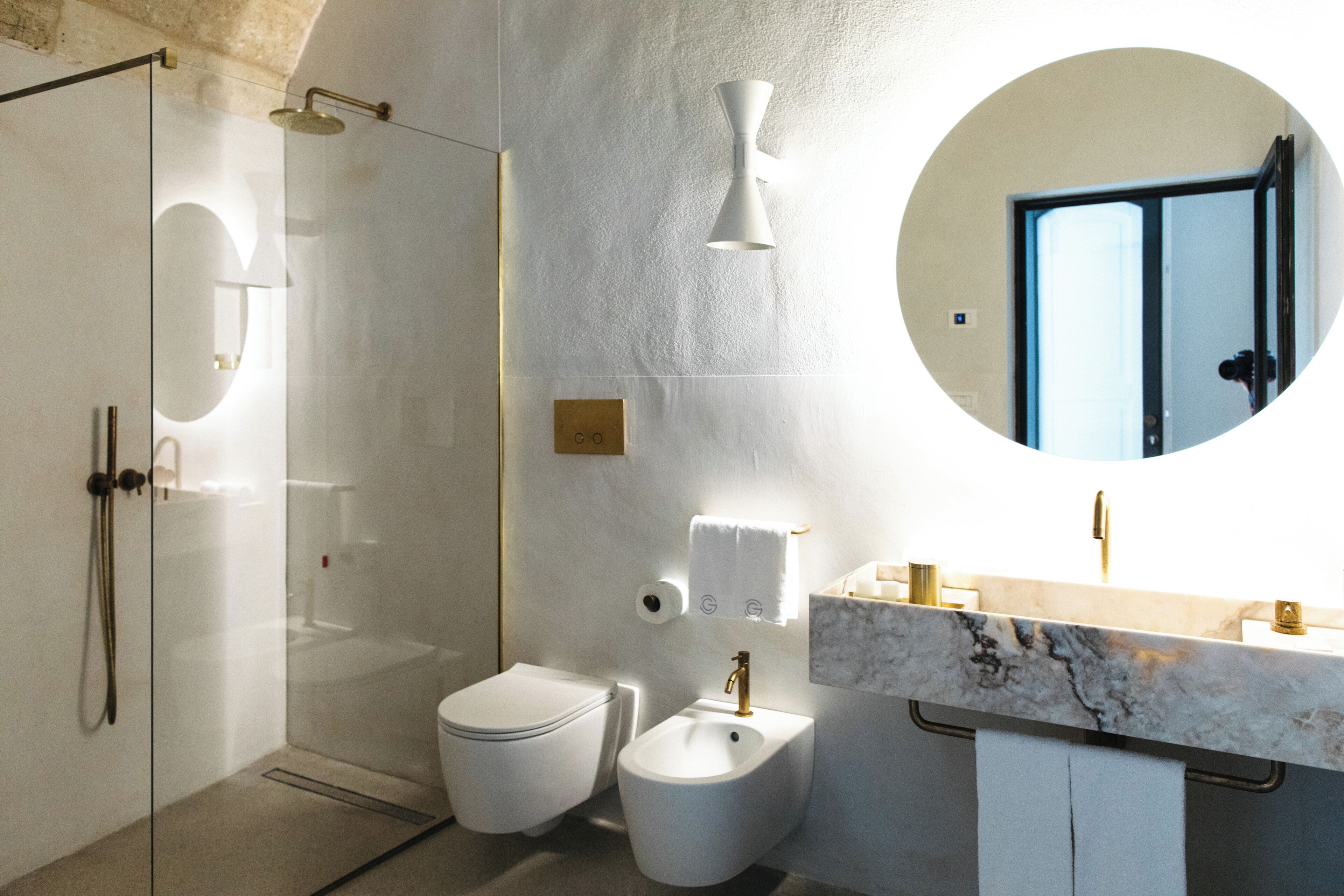 A modern bathroom with a glass-enclosed shower, a white toilet, a bidet, and a marble sink with a gold faucet.