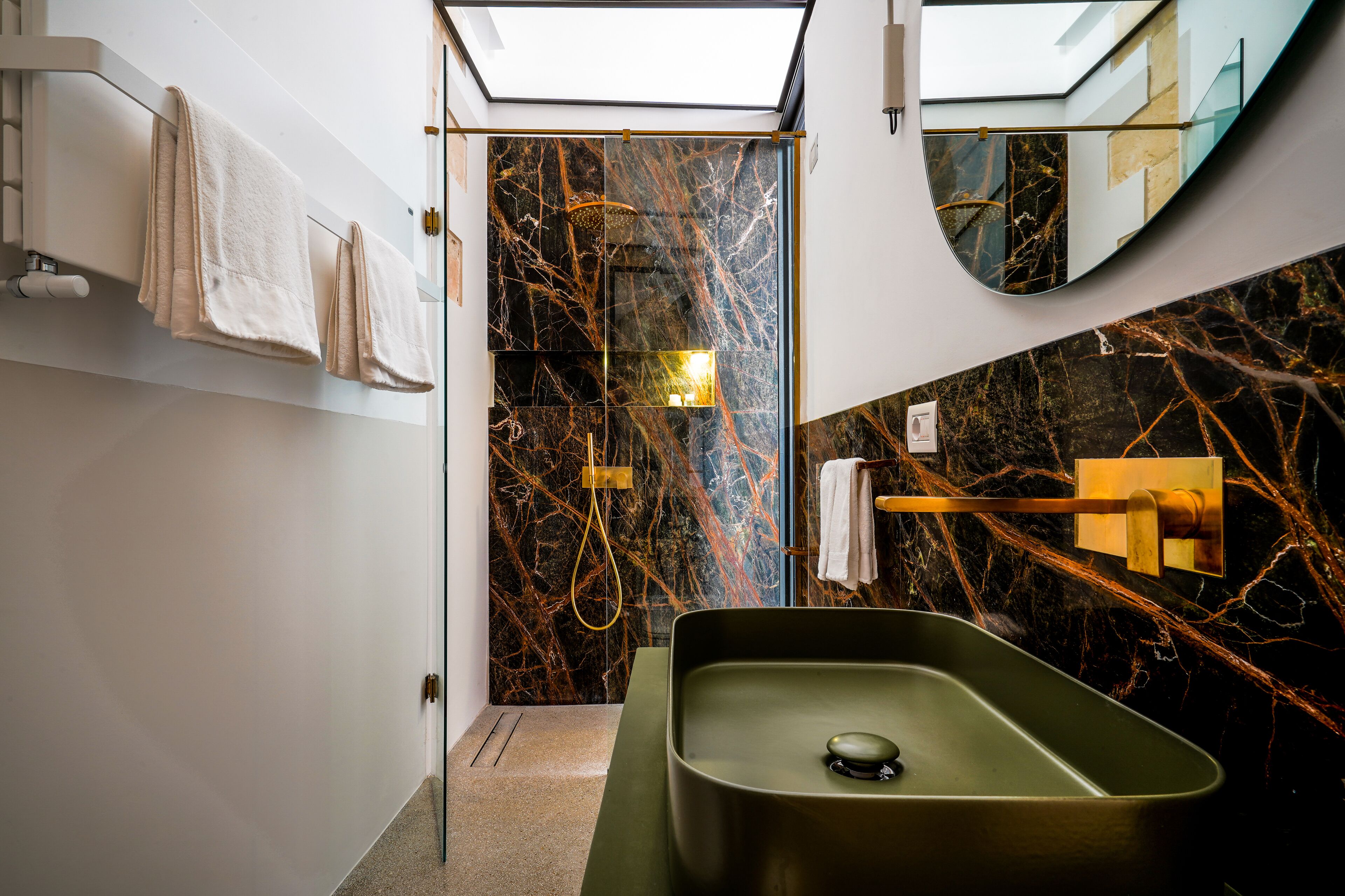Un baño moderno con un lavamanos verde, paredes de mármol y tragaluz.