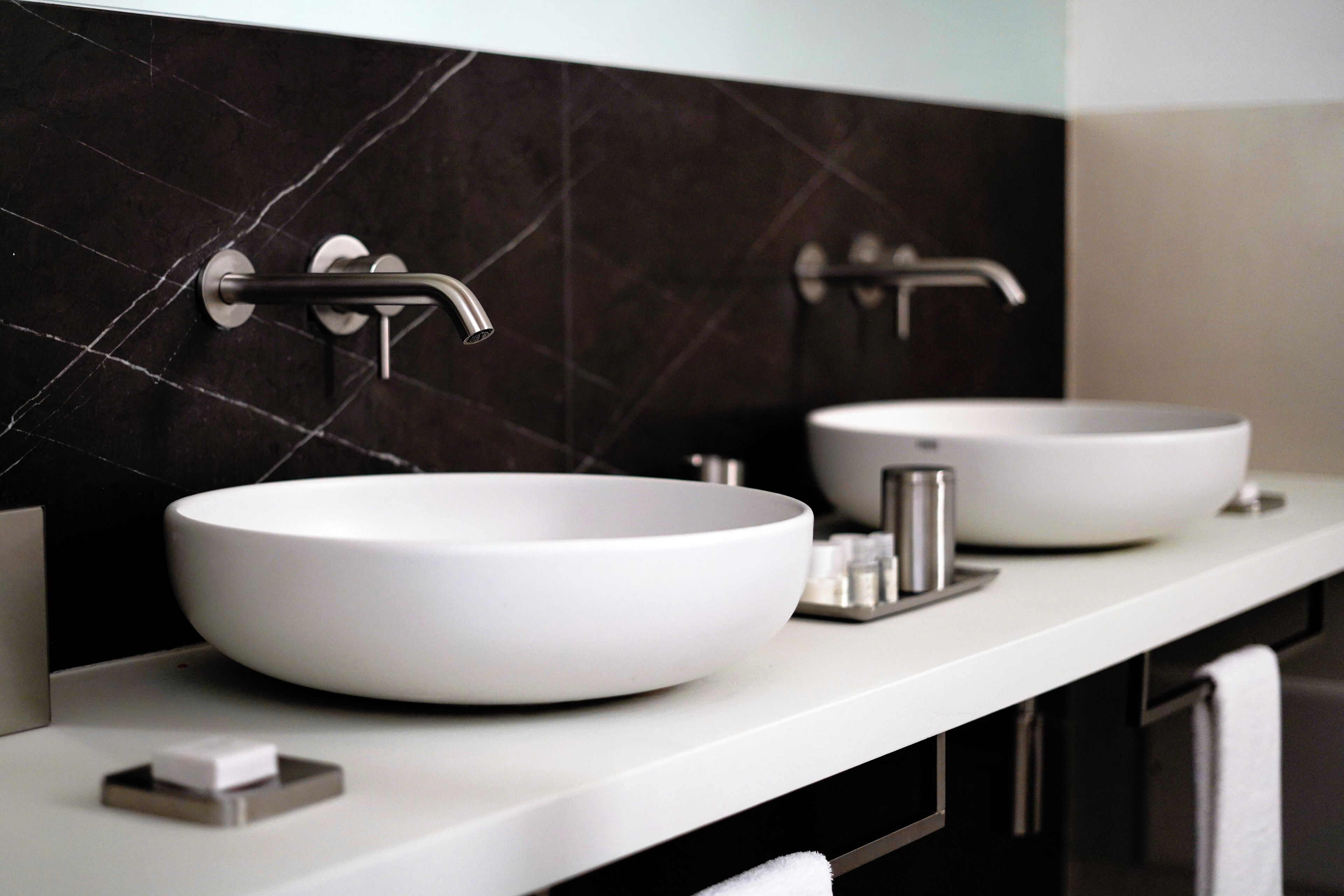 A modern bathroom with two white sinks, a black tiled backsplash, and a white countertop.