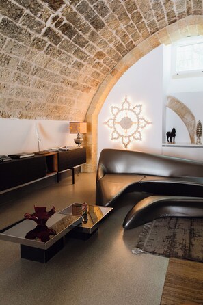 A modern living room with a stone arch, a leather sofa, a coffee table, and a decorative wall light. - Palazzo De Noha (Lecce)