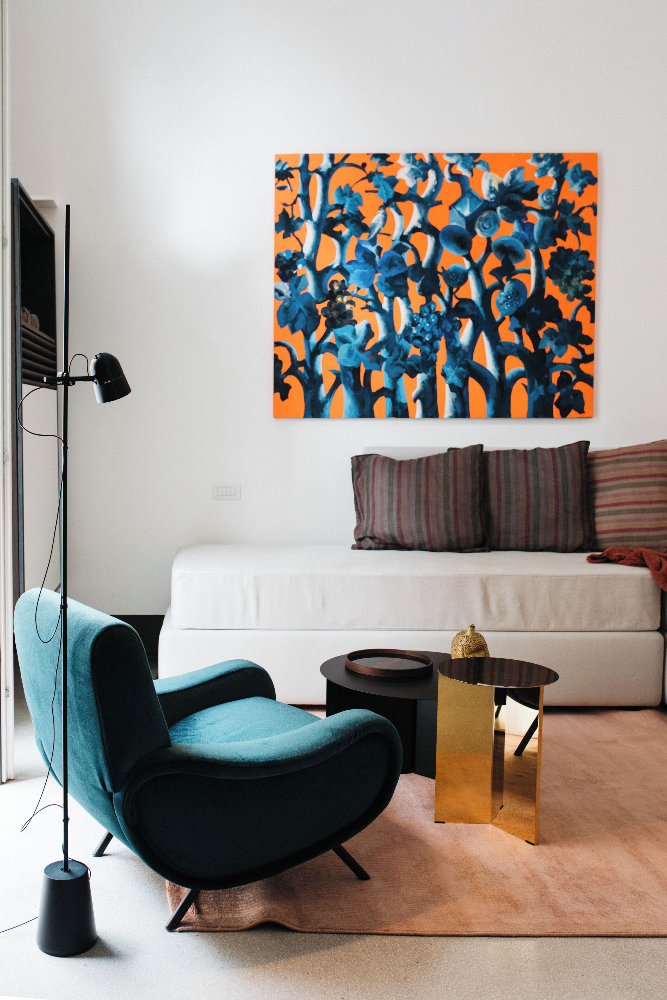 Uma sala de estar moderna com uma poltrona verde-água, um sofá branco, uma mesa de centro redonda e um grande quadro abstrato na parede.