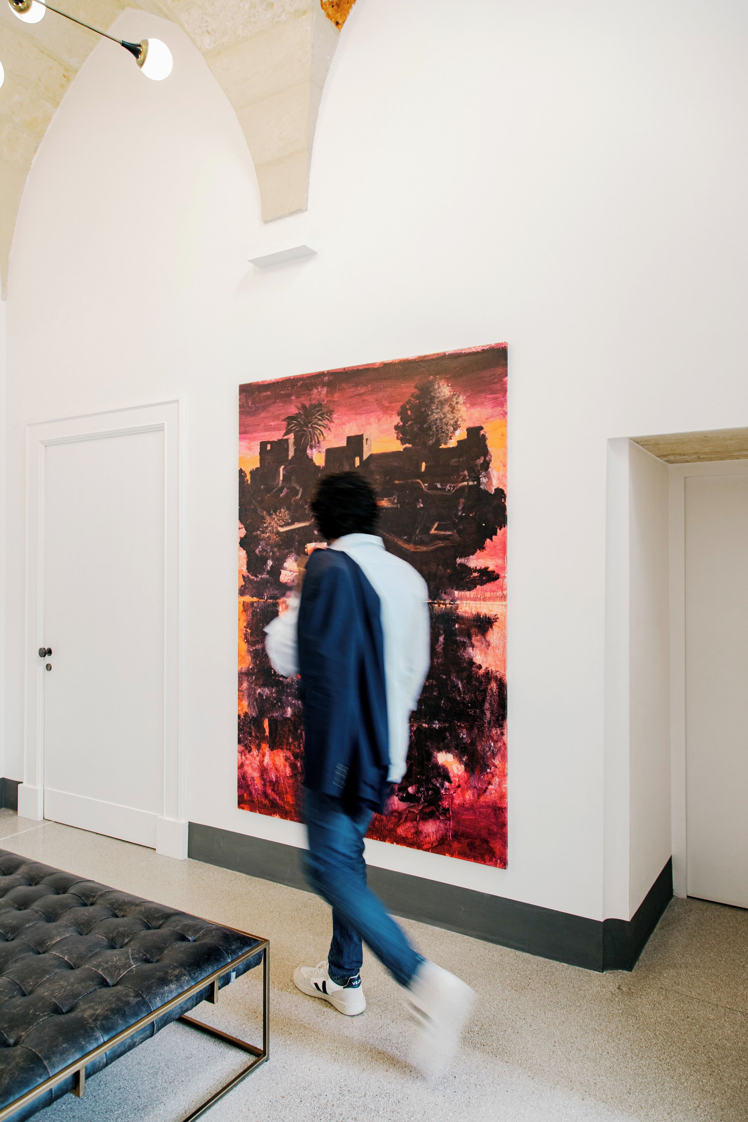 A hallway with a large abstract painting on the wall, a bench, and a door.