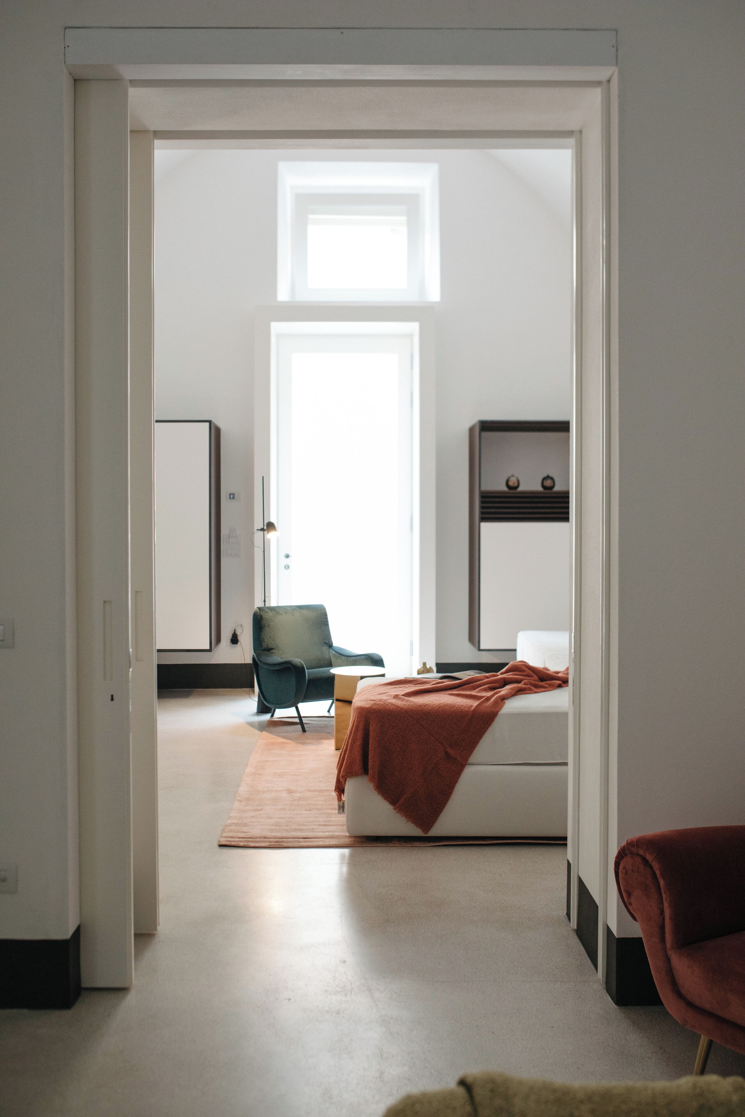 A bedroom with a bed, a chair, a wardrobe, and a large window.