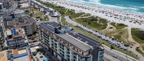 A high-rise hotel with multiple floors, a rooftop pool, and a view of the beach and ocean.