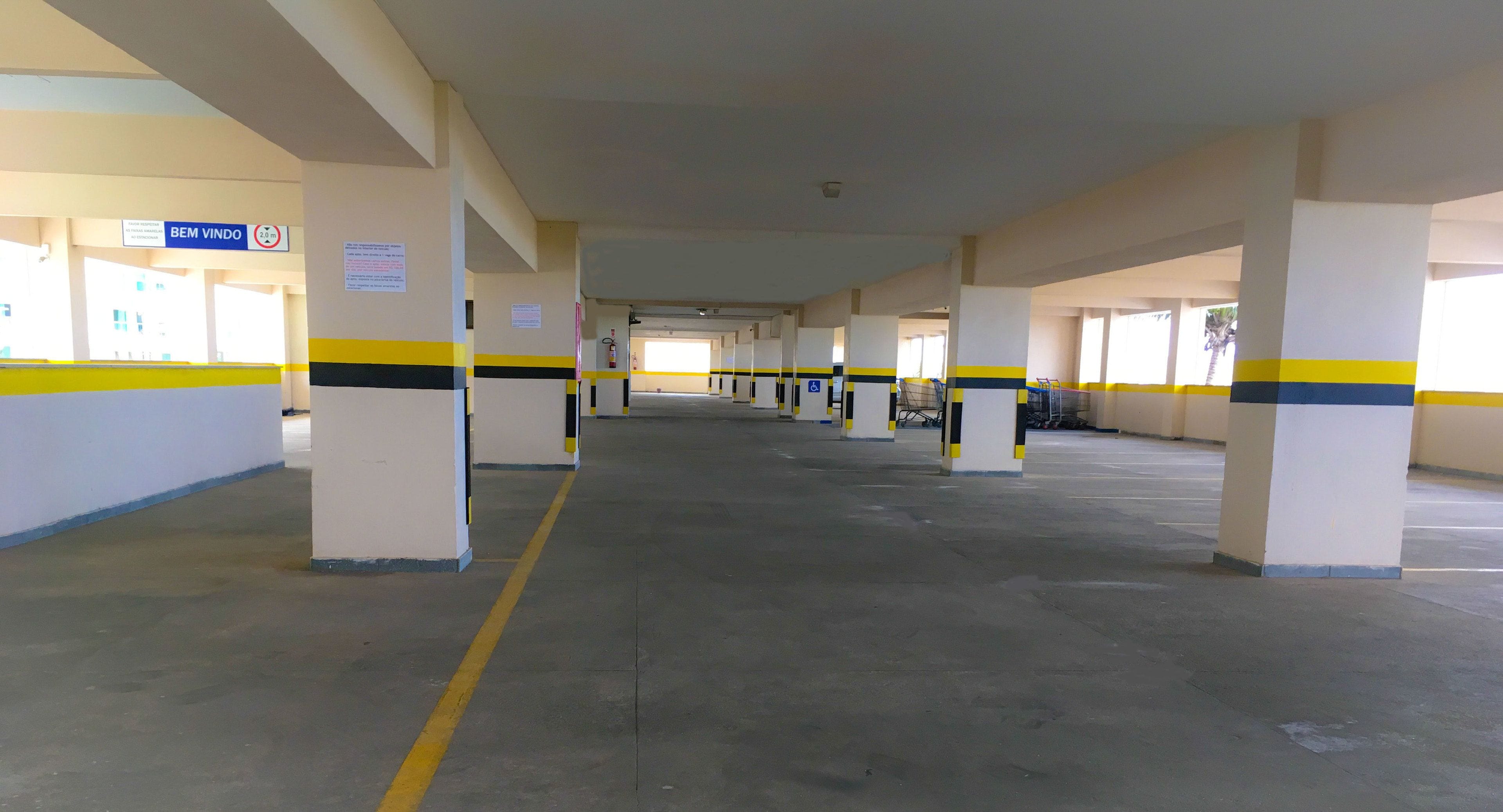 A long, empty parking garage with yellow and black striped columns and a sign reading "BEM VINDO".