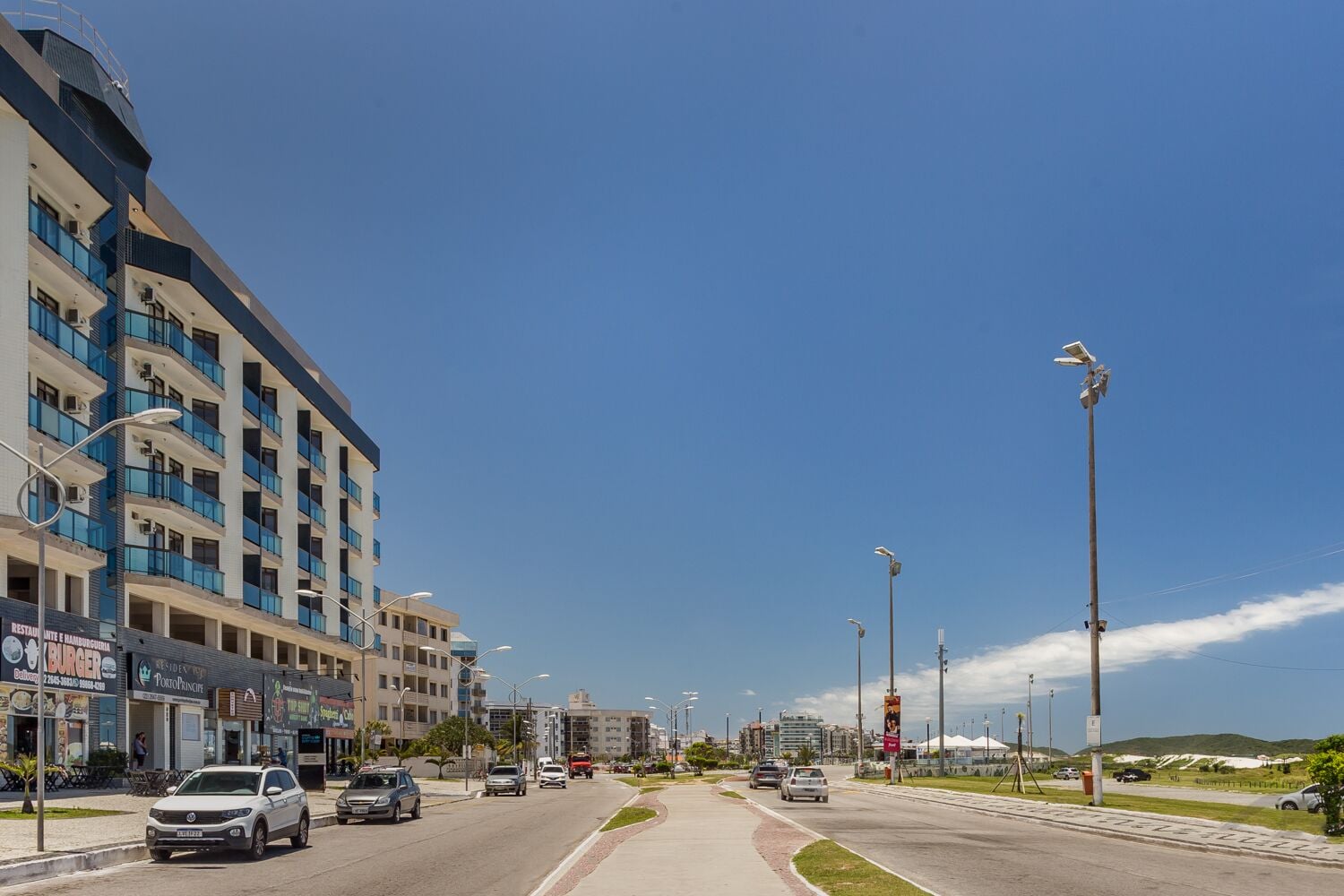 A multi-story hotel with balconies, a street with cars, and a clear blue sky.
