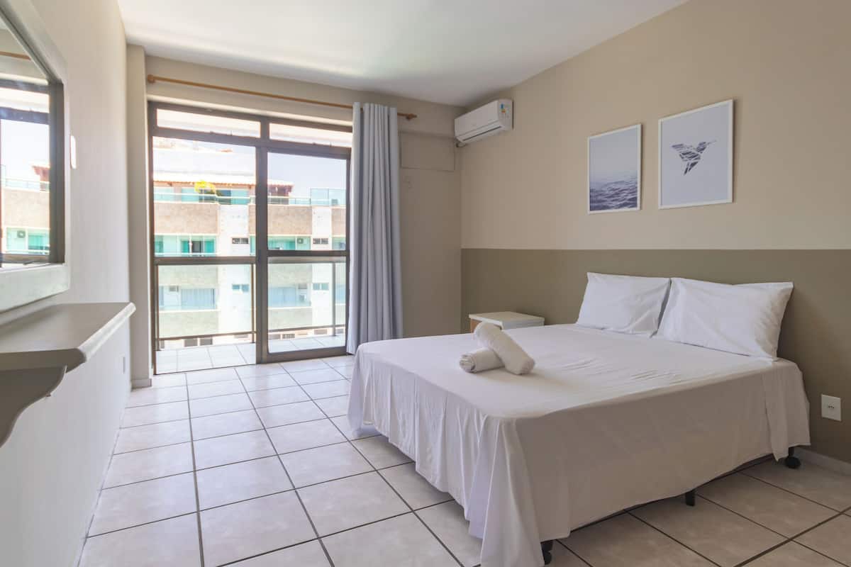 A hotel room with a large bed, a window with curtains, a bedside table, and two framed pictures on the wall.