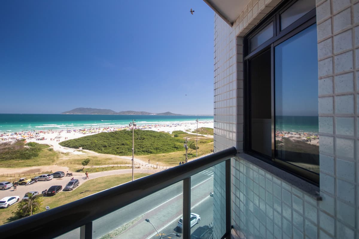 A balcony with a view of a beach, a road, and parked cars.