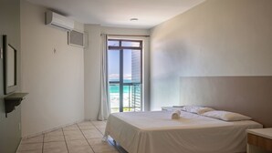 Ein Hotelzimmer mit Bett, Nachttisch, Fenster mit Meerblick und einem Balkon.