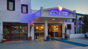 L’extérieur de l’hôtel Anil Beach se distingue par un grand panneau lumineux, de larges portes vitrées et des plantes en pot disposées devant l’entrée.