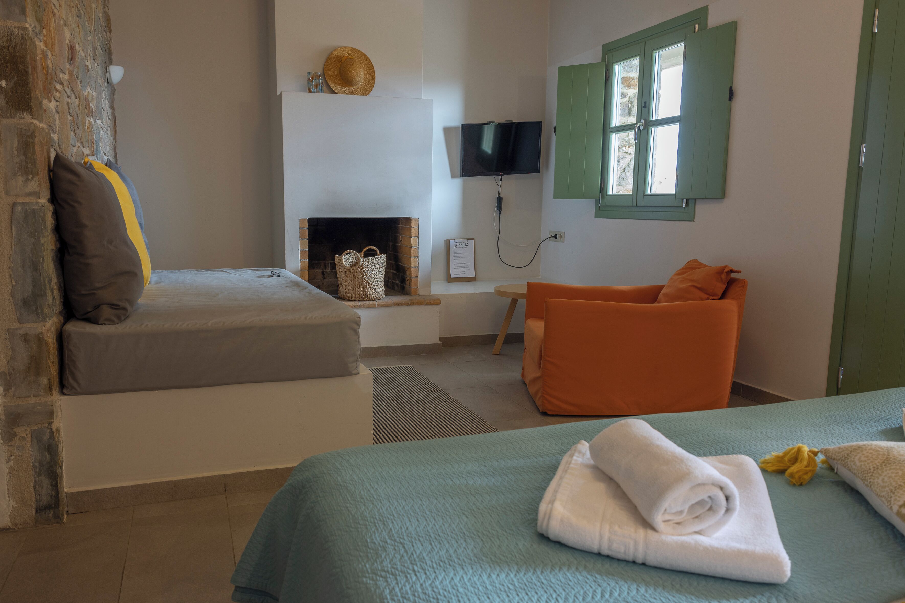 A bedroom with a bed, a sofa, a TV, a fireplace, and a window with shutters.