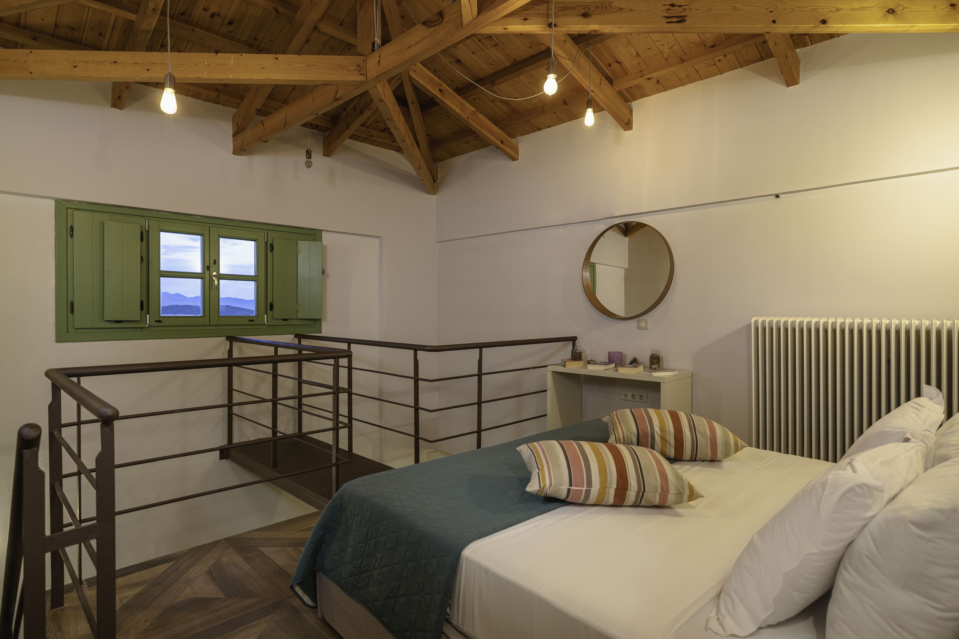 A bedroom with a bed, a window with green shutters, a round mirror, and a radiator.