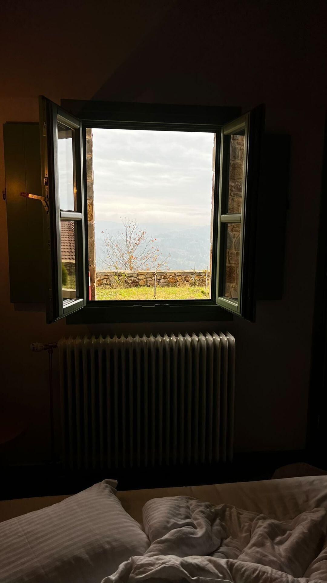 Un dormitorio con ventana que da a un paisaje rural, un radiador debajo de la ventana y una cama con edredón blanco.