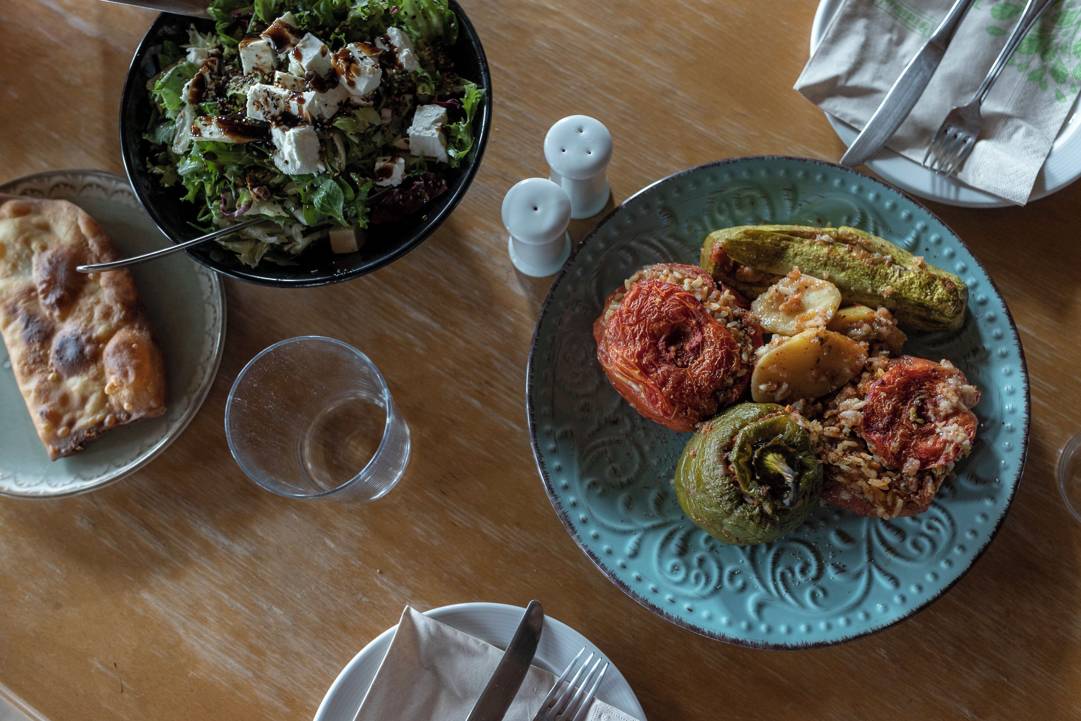 Una mesa con ensalada, pimientos rellenos y un trozo de pan plano.