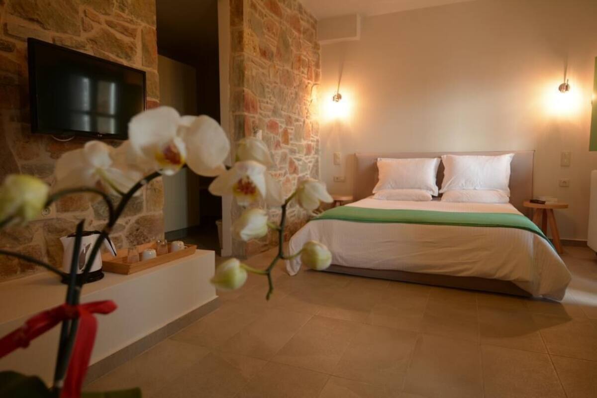 A bedroom with a stone wall, a bed with white bedding, a green throw, and a flat-screen TV mounted on the wall.