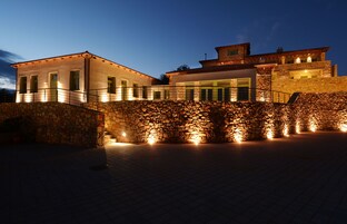 Un edificio moderno con fachada de piedra y varias ventanas, que presenta una pared de piedra y un área pavimentada al frente.