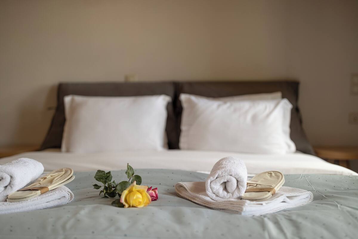 A neatly made bed with white linens, a pair of shoes, a yellow rose, and a folded towel on a bed with a light green bedspread.