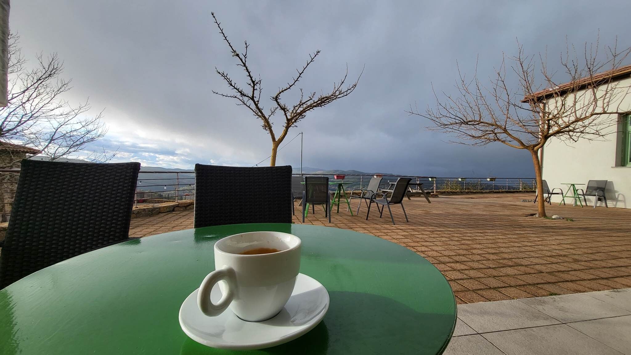 A table with a cup of coffee, outdoor seating, and a view of the sea.