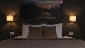 A bed with a headboard, two wall-mounted lamps, and a painting of a landscape above the bed. - De Kastanjefabriek (Eibergen)