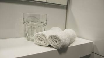Un estante blanco en el baño con un vaso transparente y dos toallas blancas enrolladas.