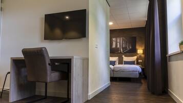 A hotel room with a bed, a desk with a chair, a TV, and a nightstand with a lamp.