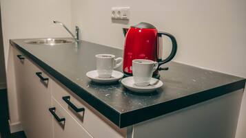 En køkkenbordplade med en rød kaffemaskine, to hvide kopper og en vask.