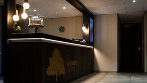 A reception desk with a dark wood finish and a golden tree silhouette. There are three pendant lights above the desk, and a clock is visible on the wall. - De Kastanjefabriek (Eibergen)
