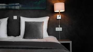 Un dormitorio con cama, mesita de noche, lámpara de pared y un cuadro sobre la cama.