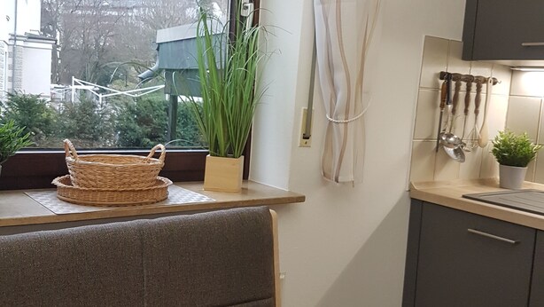 Et køkken med et vindue, en plante, en flettet kurv og en gardin.