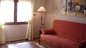 Un salon avec un canapé rouge, une lampe sur pied, une fenêtre avec des rideaux et un tableau accroché au mur.