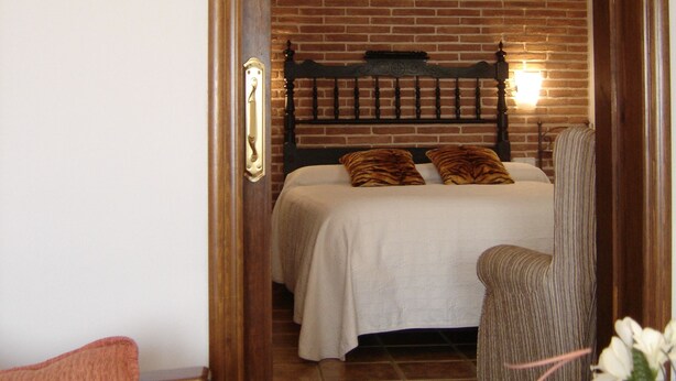 Une chambre avec un mur en briques, un cadre de lit en bois, une couvre-lit blanche et une chaise avec un coussin à rayures.