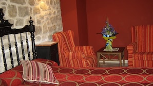 Une pièce comprenant un lit, deux fauteuils à rayures, une petite table et un vase de fleurs.