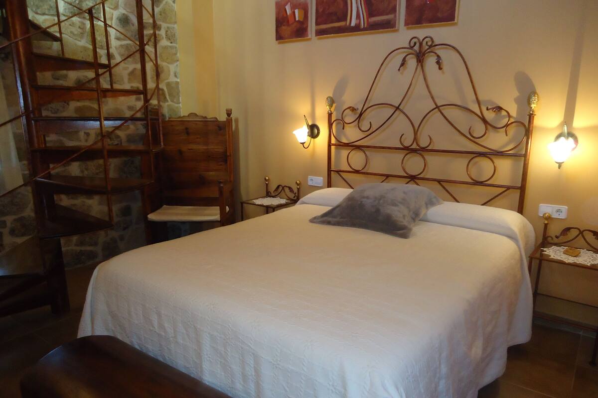 Ein Schlafzimmer mit einem Bett, einem Sessel, einem kleinen Tisch und einer Treppe.