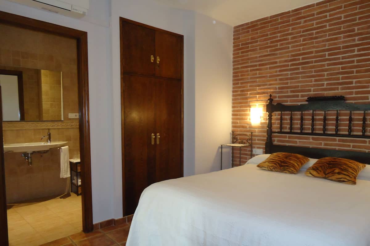 Ein Schlafzimmer mit Bett, einem Holzschrank, einem Badezimmer mit Waschbecken und einer Ziegelwand.
