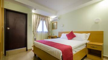 A hotel room with a bed, bedside table, nightstand, and an air conditioning unit.