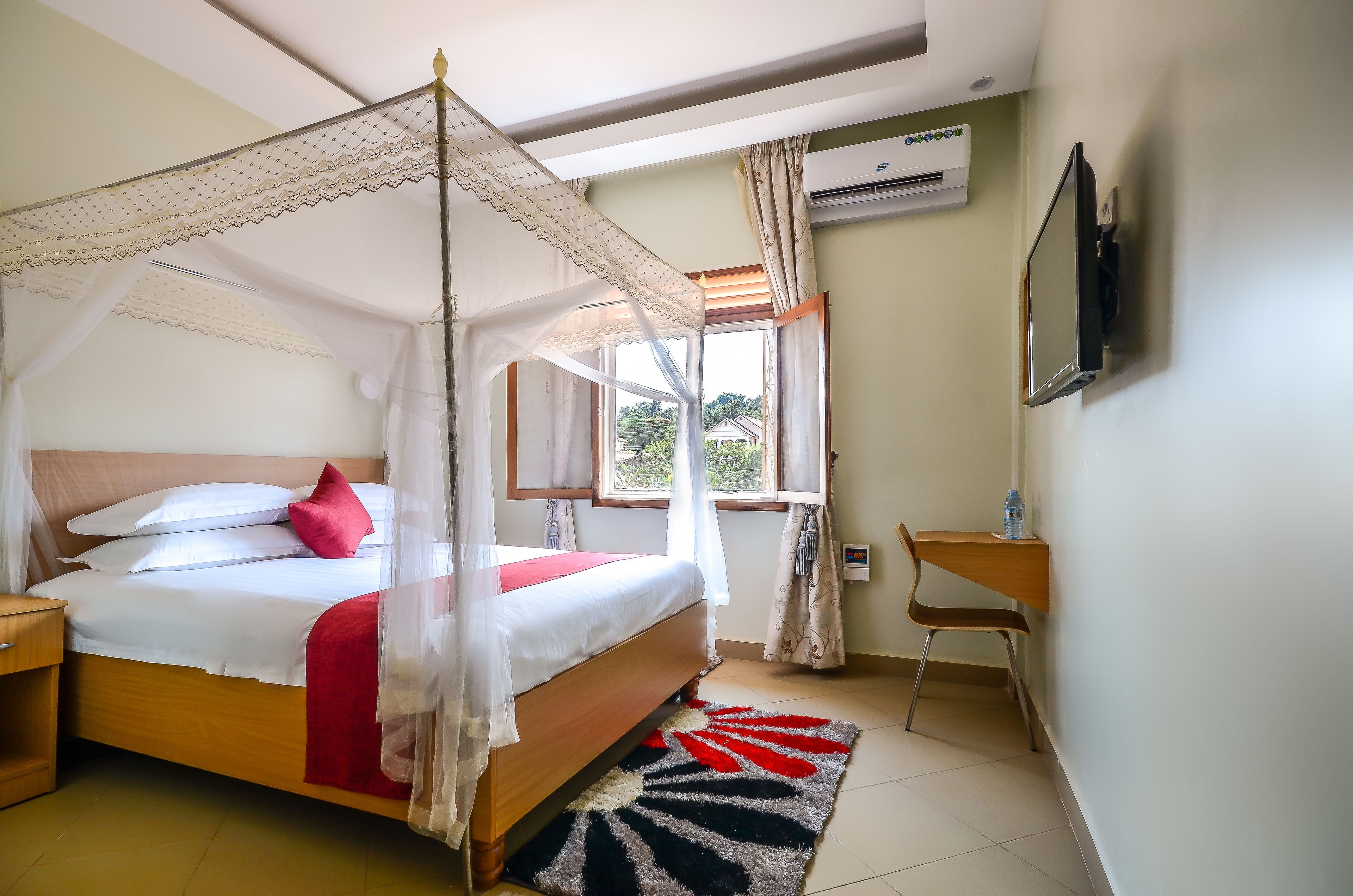 A bedroom with a bed, a bedside table, a chair, a TV, and an air conditioning unit.