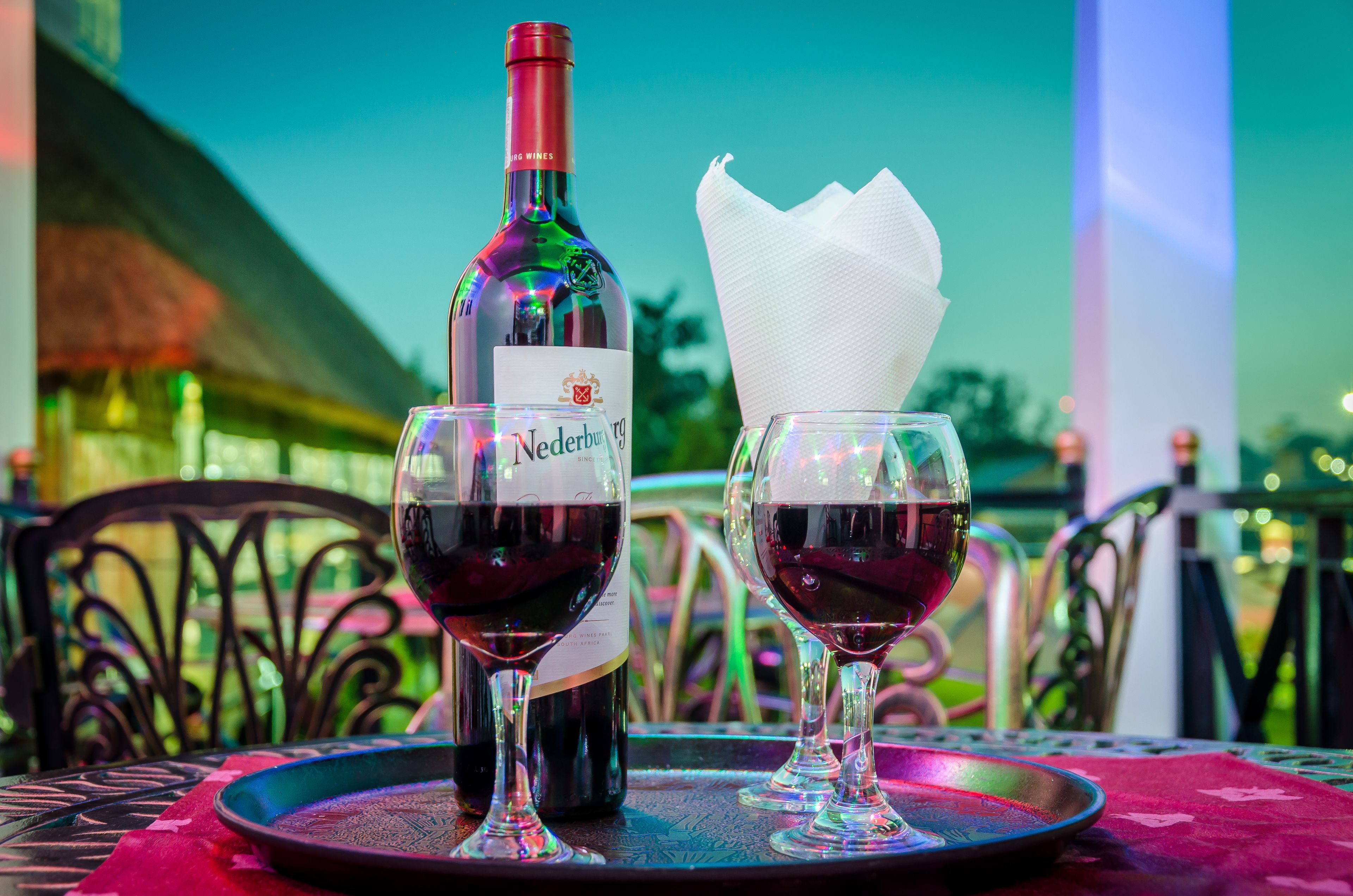 Une bouteille de vin Nederburg et deux verres sur une table recouverte d’une nappe rouge.