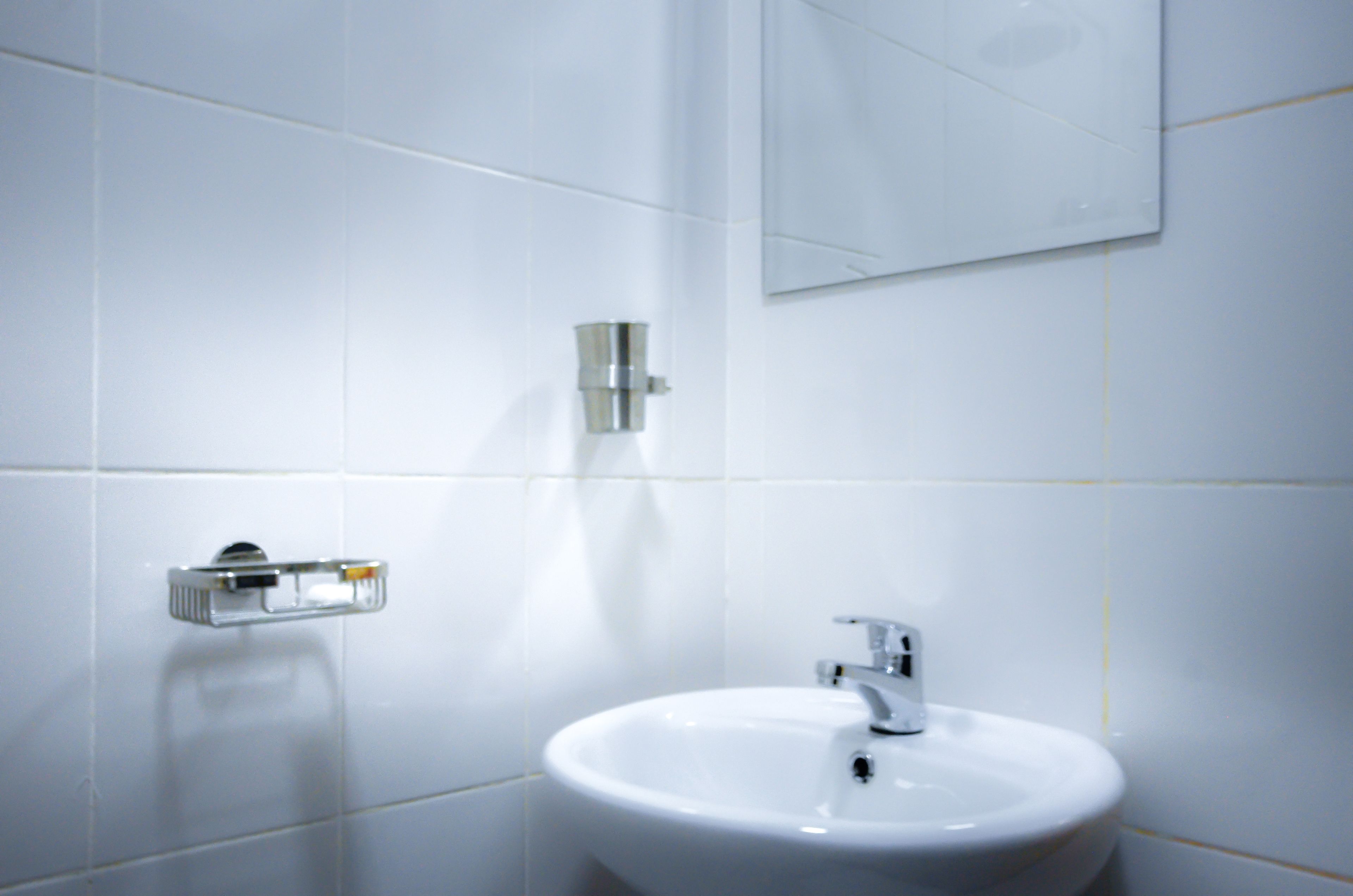 Une salle de bain avec des carreaux blancs, un lavabo et un miroir.