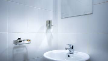 Une salle de bain avec des carreaux blancs, un lavabo et un miroir.
