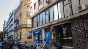 A row of parked motorcycles in front of a building with a stone facade and a blue sign.