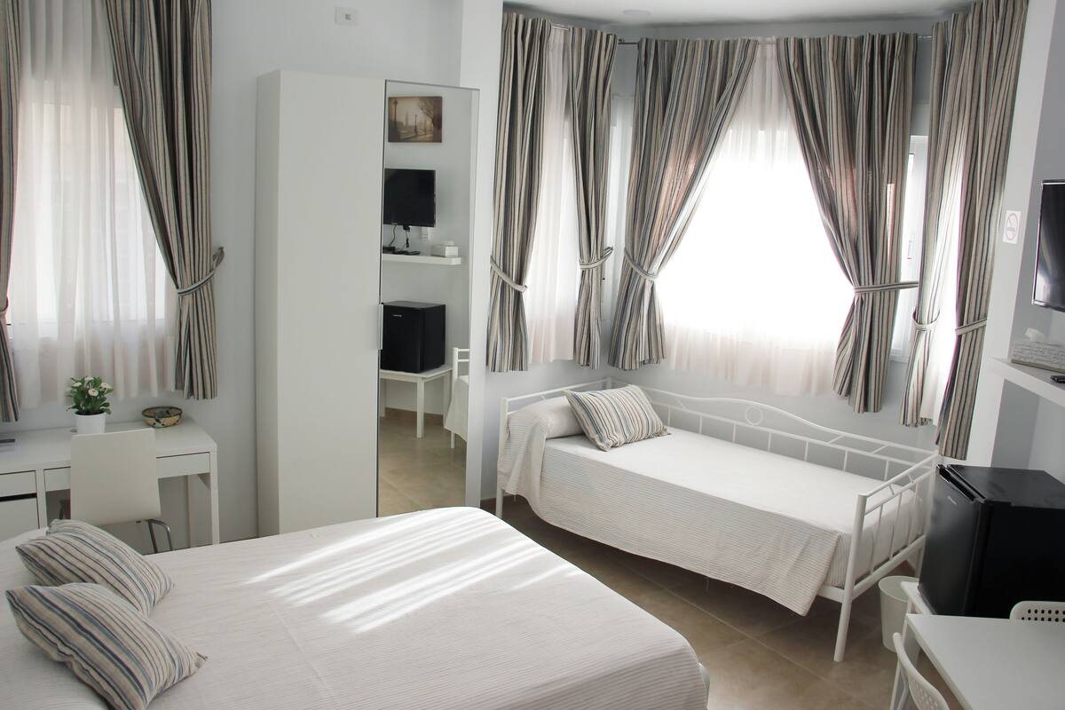 A hotel room with a large bed, a smaller bed, a desk, a chair, a TV, and a wardrobe.