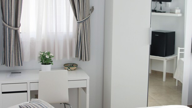 A bedroom with a bed, a desk, a chair, a wardrobe, and a television.
