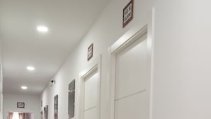 A hotel corridor with white doors, a bed with curtains, and a security camera.