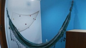 A room with a hammock against a blue wall, a wooden cabinet, and a small stool. - Pousada Melodia do Mar (Cabo Frio)