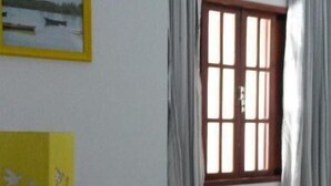 A room with a wooden desk, a window with curtains, and a framed picture on the wall. - Pousada Melodia do Mar (Cabo Frio)